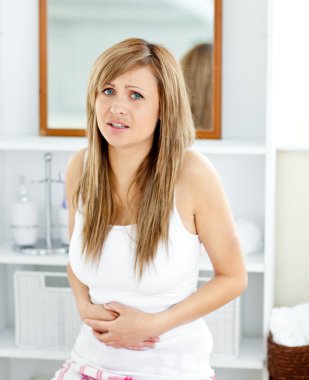 Blond woman having a stomachache in her bathroom clipart