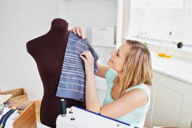 Delighted young woman sewing clothes at home clipart