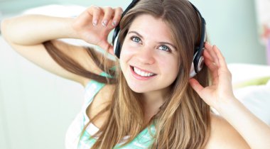 Cheerful caucasian girl listening to music sitting on a sofa clipart