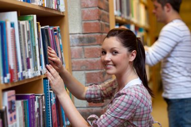 Joyful young woman looking for a book clipart