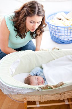 Young mother looking at her little son sleeping in his bed clipart