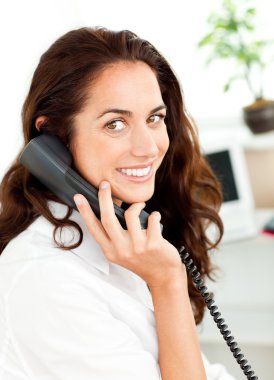 Lively young businesswoman talking on phone sitting at her desk clipart