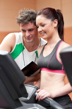 Joyful female athlete standing on a running machine with her per clipart