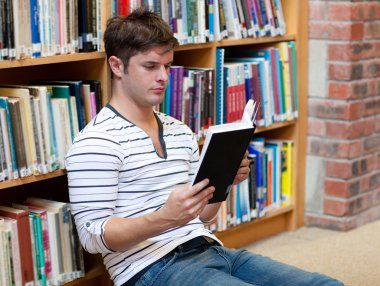 Handsome young man reading a book stting on the floor clipart