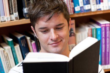 Portrait of a smiling male student reading a book sitting on the clipart