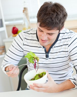 Delighted young man eating a healthy salad in the kitchen clipart