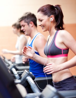 Beautiful female athlete standing on a running machine listening clipart