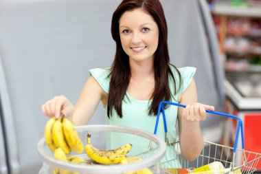 Healthy woman with shopping-basket buying bananas in a grocery s clipart
