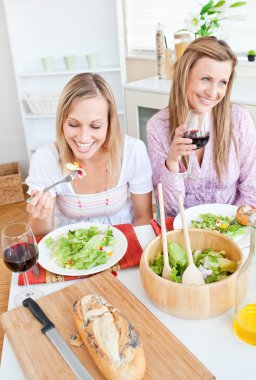 Two delighted female friends eating salad in the kitchen clipart