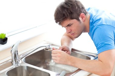 Concentrated man repairing his sink in the kitchen clipart