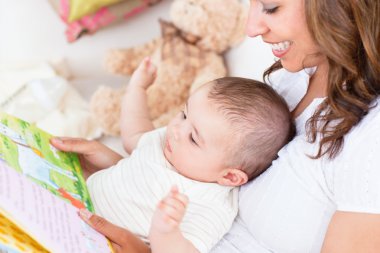 Joyful mother showing images in a book to her cute little son clipart