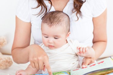 Attentive mother showing images in a book to her cute little son clipart