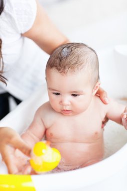 Adorable baby taking a bath wihile his adorable mother takes car clipart
