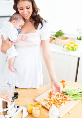 Radiant mother preparing food for her adorable baby in the kitch clipart