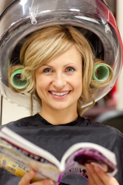 Delighted woman reading a magazine with hair curlers under a hai clipart