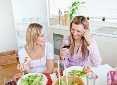 Two women in the kitchen chatting and eating salad with glasses clipart