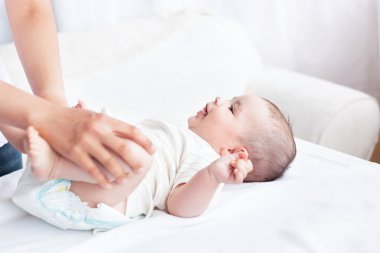 Cute baby smiling while his mother is changing his nappy in the clipart