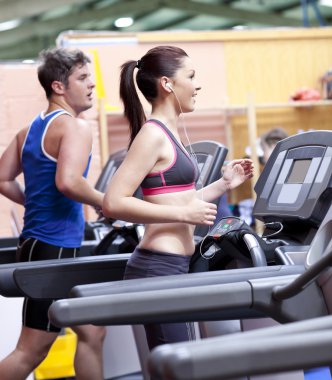 Healthy couple running on a treadmill in a sport centre clipart