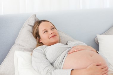 Thoughtful pregnant woman resting on a bed clipart