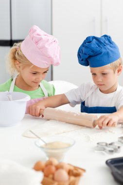 Little girl looking at her serious brother using a rolling pin clipart