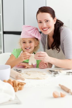 Happy girl with her mother baking little cakes clipart