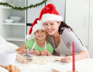 Portrait of a cute girl with her mother baking Christmas cookies clipart