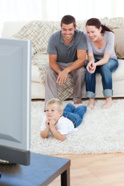 Cute little boy watching television on the floor with his parent clipart