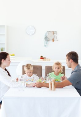 Family holding their hands while praying before eating a salad clipart