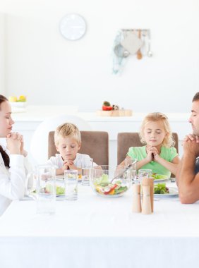 Parents and their children praying during their lunch clipart