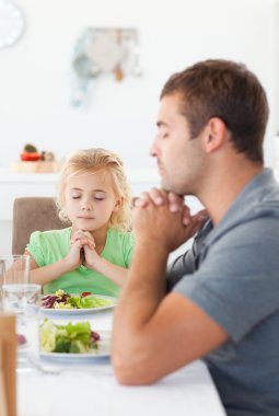 Concentrated father and daughter praying before eating their sal clipart