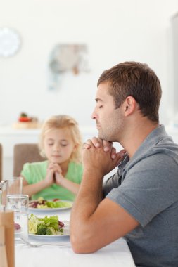 Adorable father and daughter praying during the lunch clipart