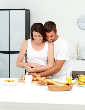 Happy couple hugging while preparing their breakfast together clipart