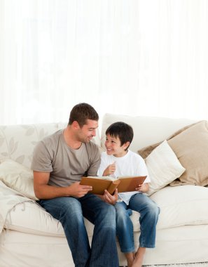 Adorable boy looking at a photo album with his father on the sof clipart