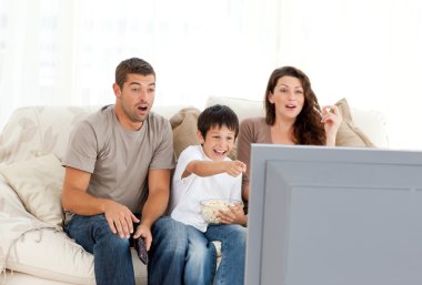 Happy family watching a movie on television together on the sofa clipart