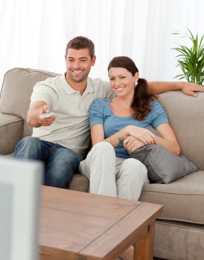 Happy man changing channel while watching television with his wi clipart