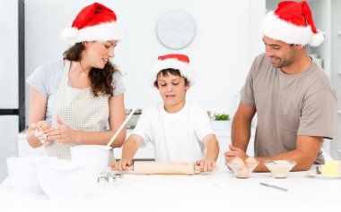 Proud parents looking at their son using a rolling pin clipart