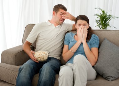 Scared couple eating pop corn while watching a horror movie clipart