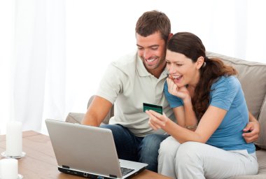 Happy couple looking at their accounts online sitting on the sof clipart