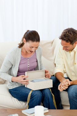 Amazed woman opening a present from his boyfriend on the sofa clipart