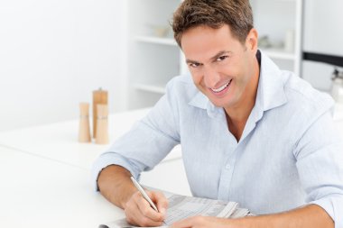 Happy man doing a crossword sitting at a table clipart
