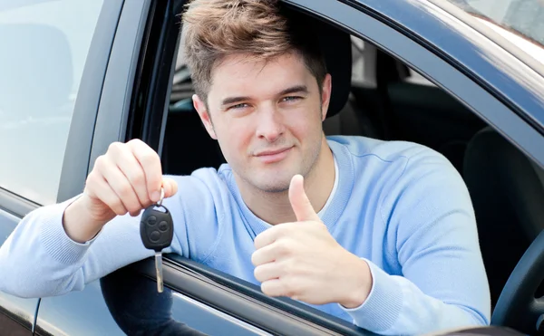 Позитивний молодий чоловік тримає ключ, сидячи в машині — стокове фото
