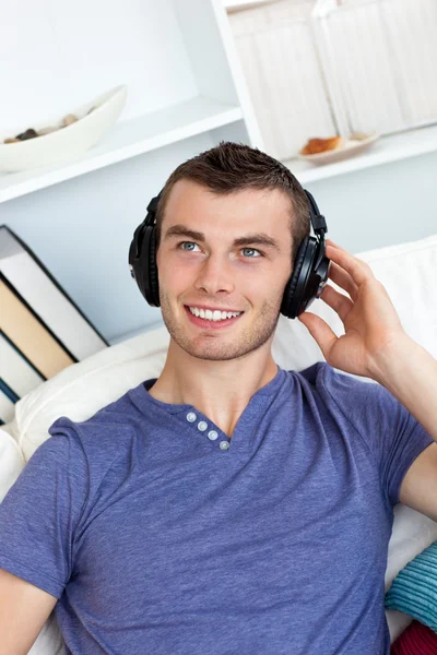 Lively young man listening to music sitting on the couch — Stock Photo, Image