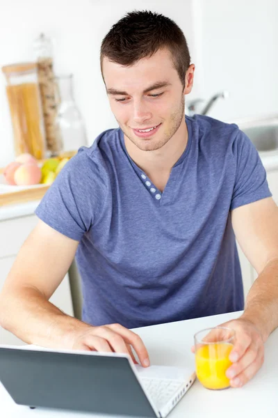 魅力的年轻人使用他持有的橙汁的笔记本电脑 — 图库照片