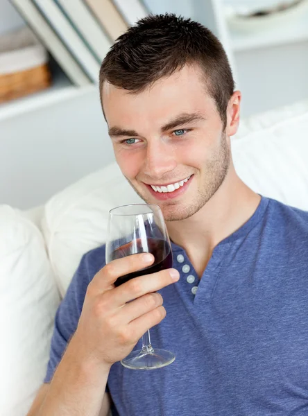 Joven animado bebiendo vino sentado en el sofá — Foto de Stock