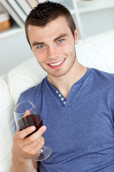 Улыбающийся молодой человек с бокалом вина, смотрящий в камеру — стоковое фото