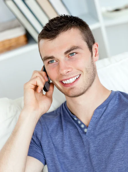 Jovem carismático falando ao telefone sentado no sofá — Fotografia de Stock
