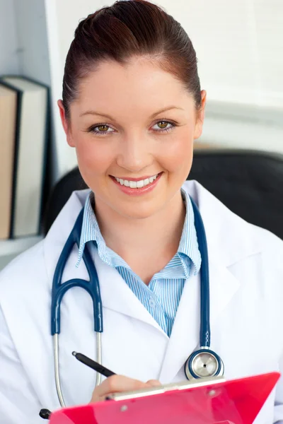 Selbstbewusste Ärztin, die in die Kamera lächelt und ein Klemmbrett hält — Stockfoto