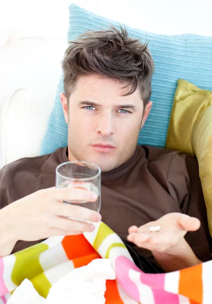 Sick caucasian man holding pills and water looking at the camera — Stock Photo, Image