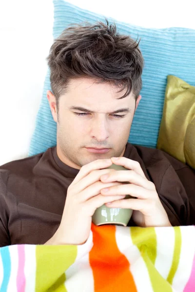Hombre deprimido sosteniendo una taza de café tumbado en el sofá —  Fotos de Stock