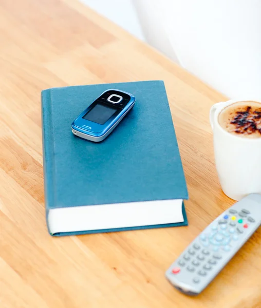 Close-up de um livro, celular, remoto e xícara de café na guia — Fotografia de Stock